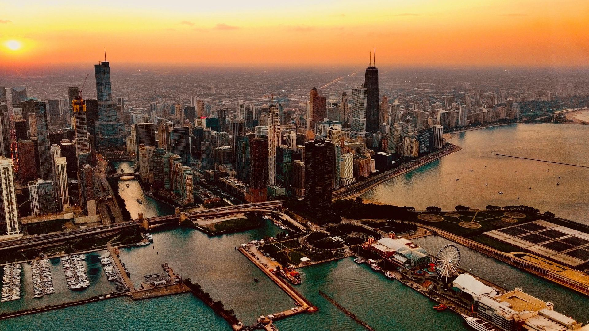 Chicago skyline at sunset, view from above water. Orange sky, skyscrapers, harbor with boats.
