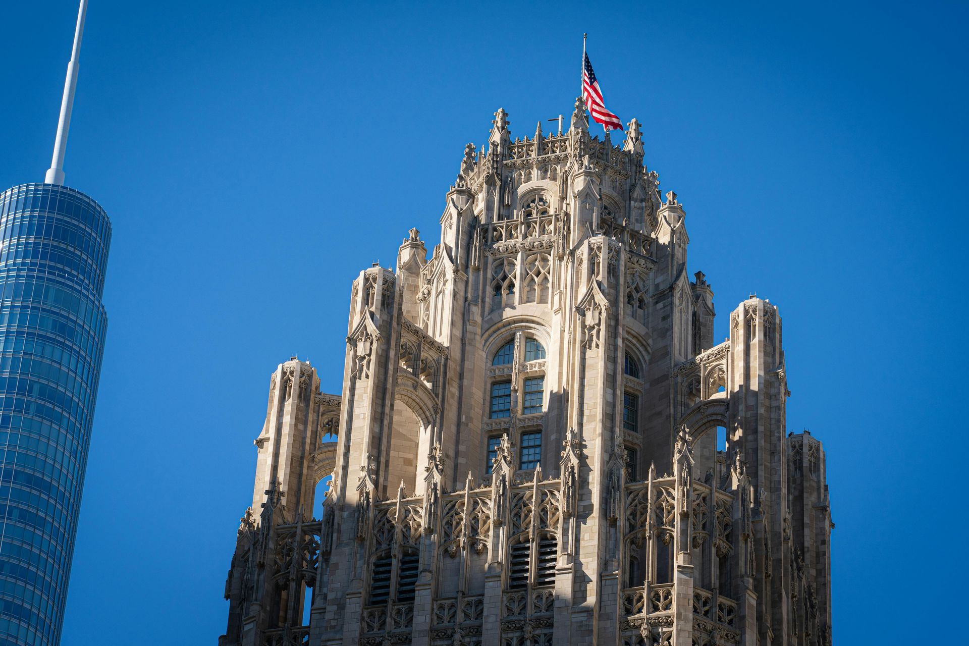 Ornate gothic skyscraper topped with an American flag against a clear blue sky.