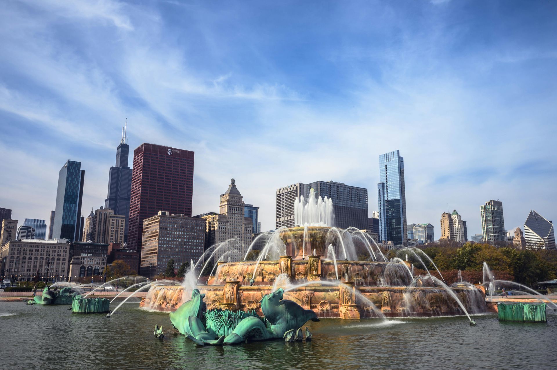Buckingham Fountain sprays water in front of Chicago skyline under a blue sky.