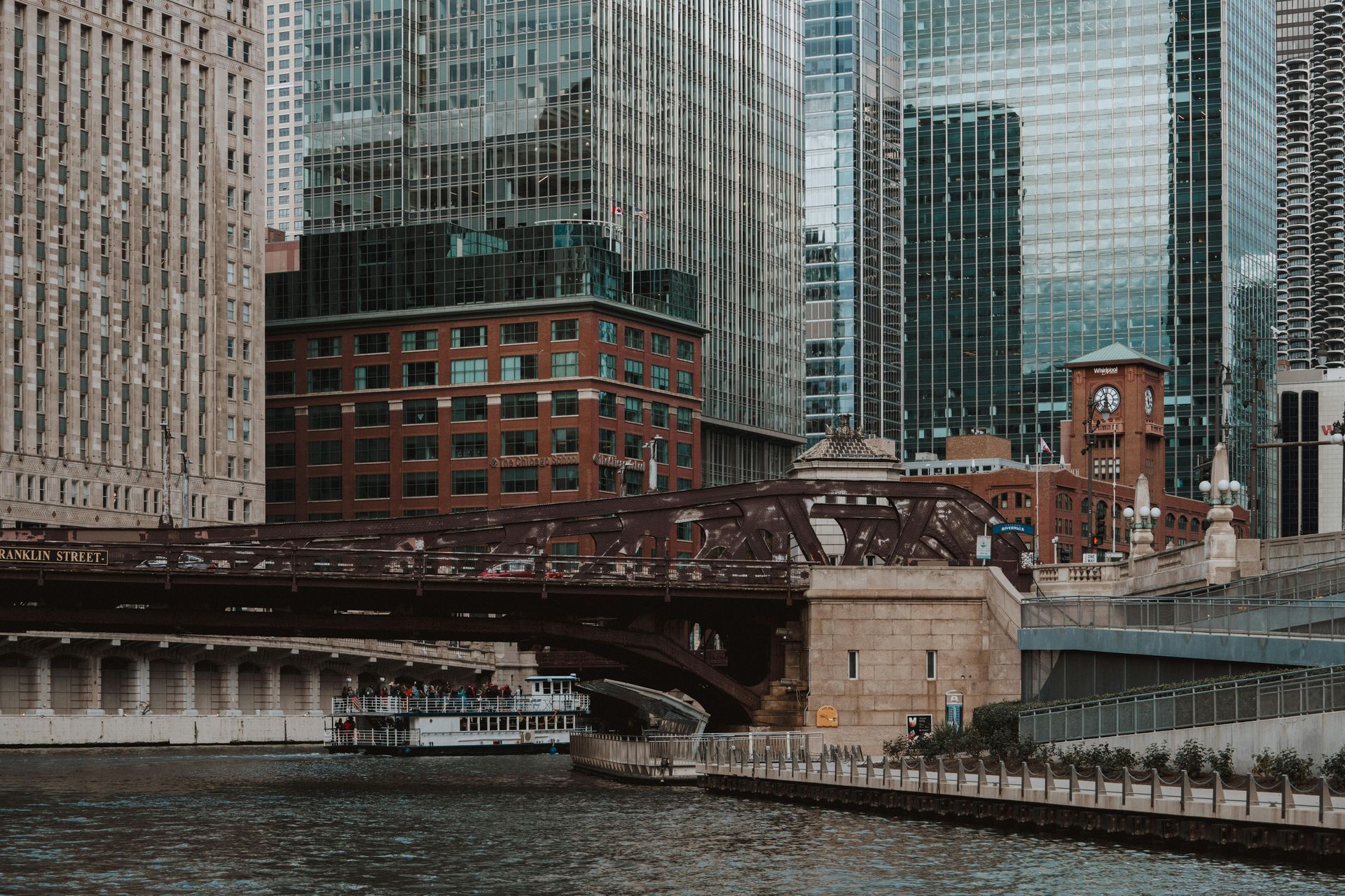 Chicago river and cityscape with boat, bridge, and tall buildings.