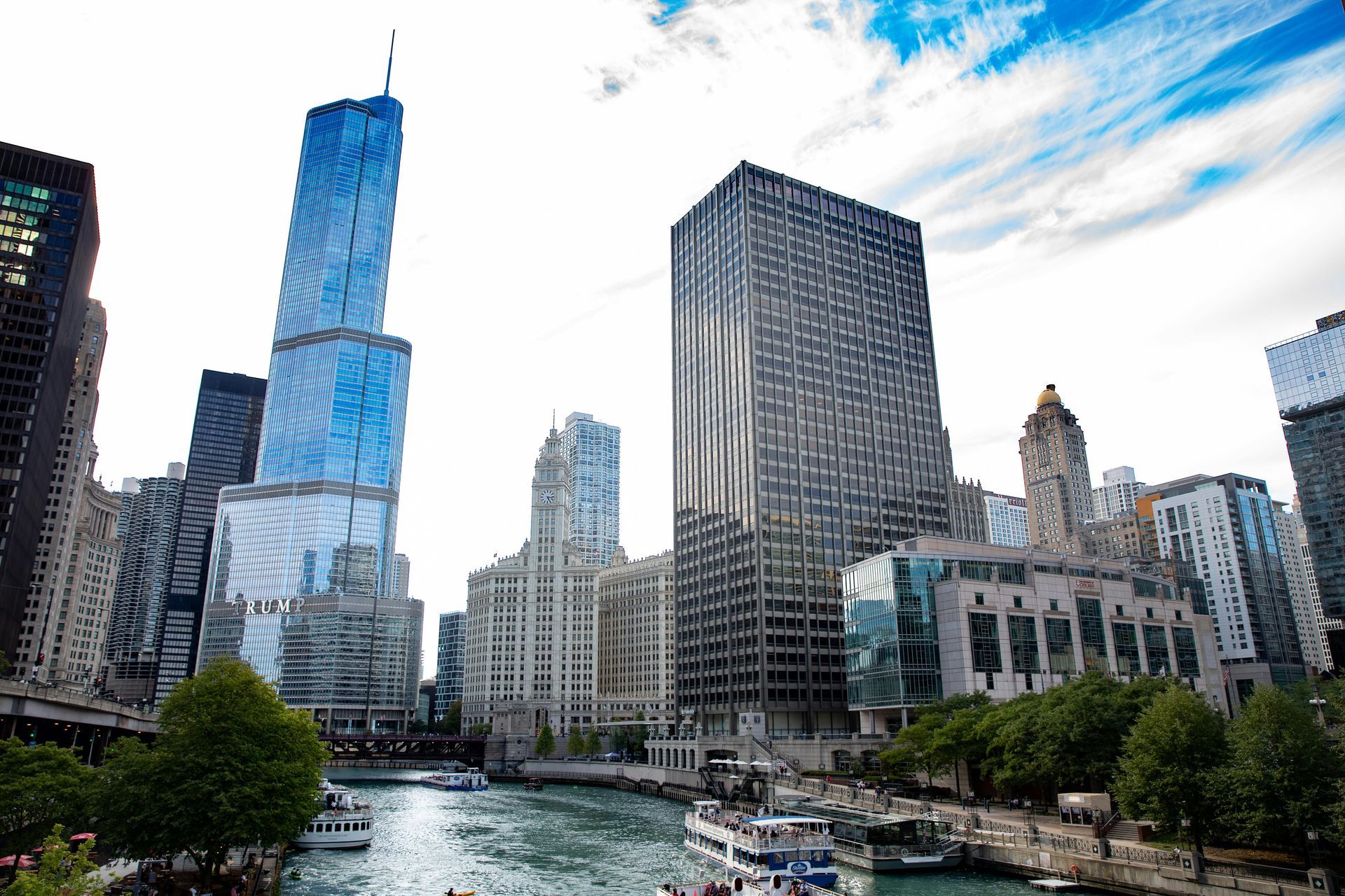 Chicago skyline view with skyscrapers, river, boats, and cloudy sky.