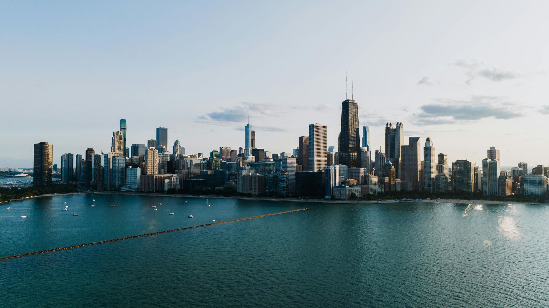 Chicago skyline at dusk over Lake Michigan. Tall buildings silhouette against a light blue sky.