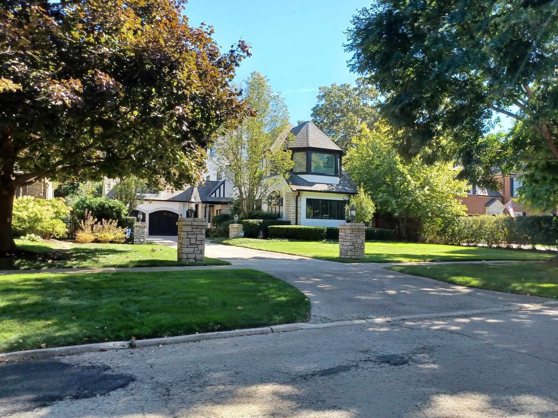 A house with a circular tower and black garage doors, reached by a circular driveway lined with pillars.