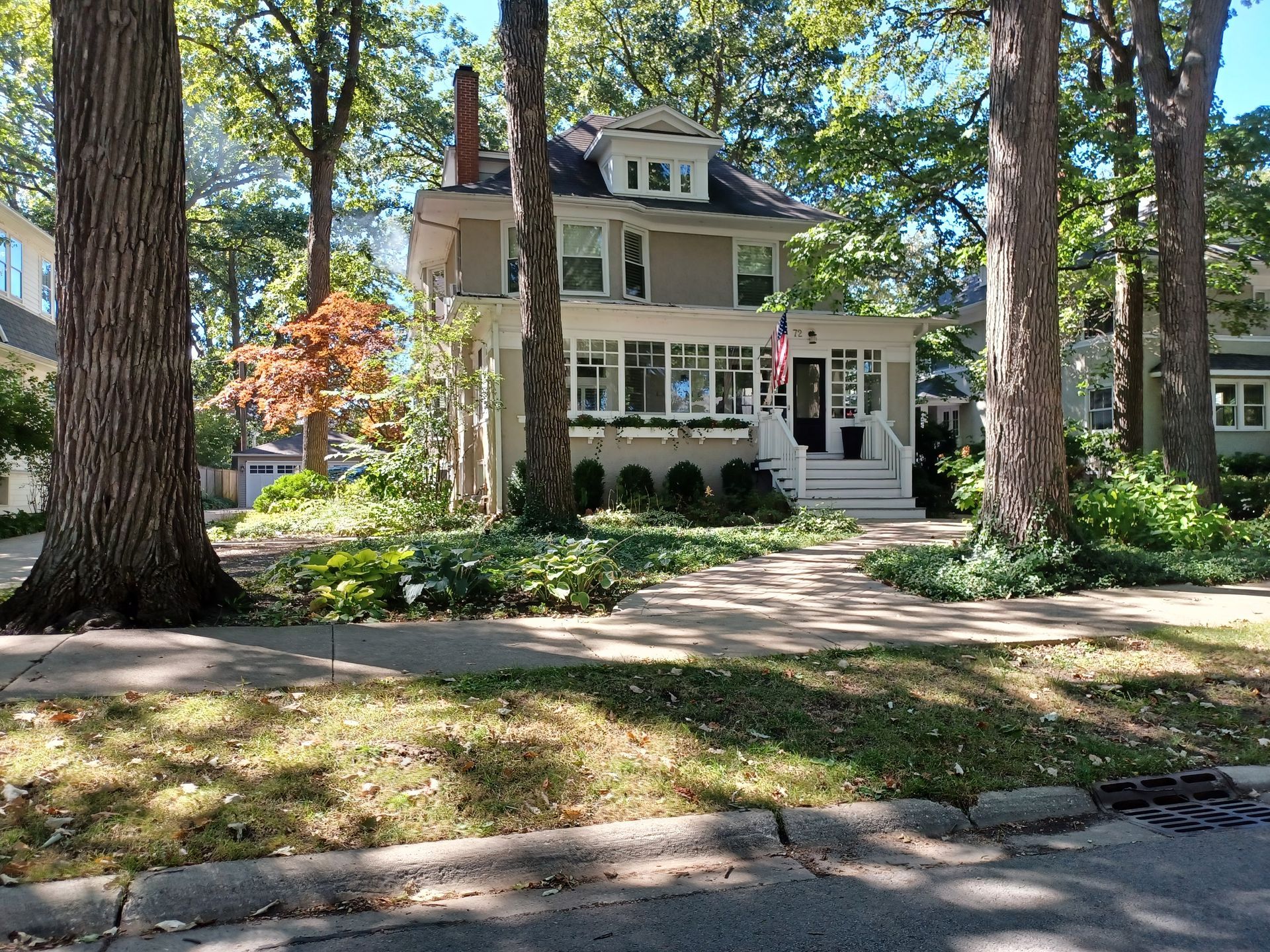 Two-story house with light beige siding, white trim, and a porch. Mature trees line the front yard.
