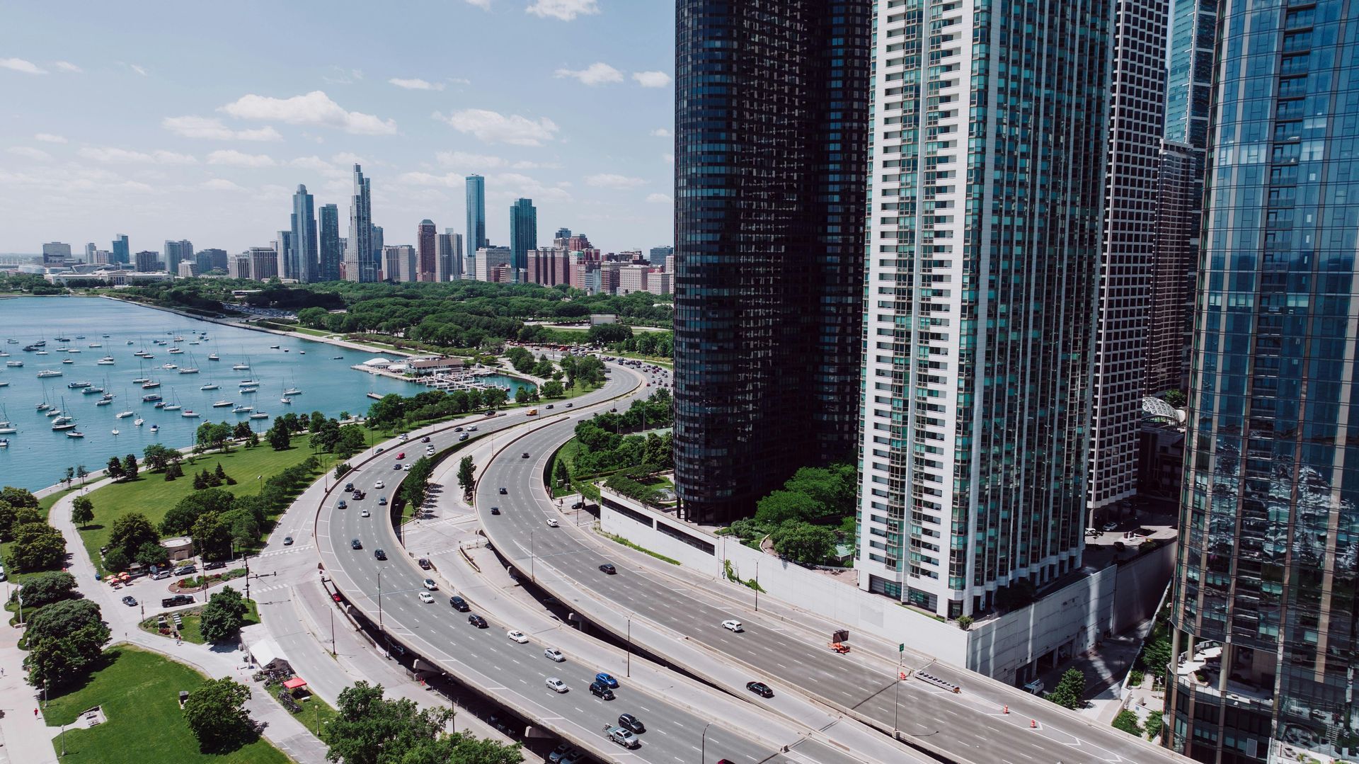 Curved waterfront highway beside tall glass skyscrapers and a bay with city skyline in the distance