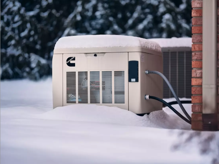 Generator covered in snow next to a brick wall and air conditioning unit.