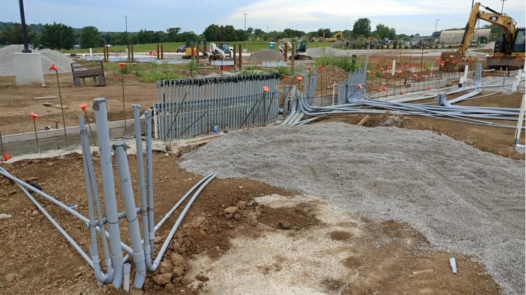 Construction site with grey pipes, gravel, and heavy machinery.