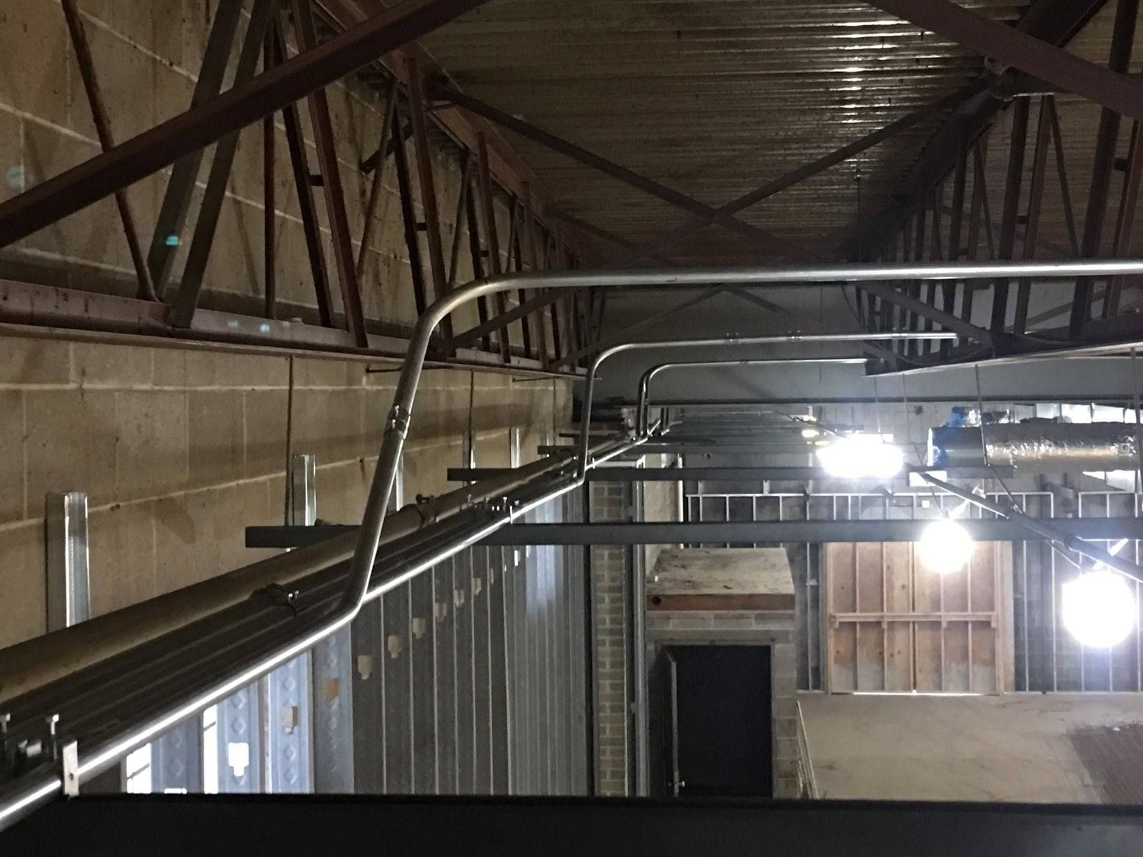 Steel beams and conduit in a building's unfinished interior; overhead view with a dark doorway at the end.