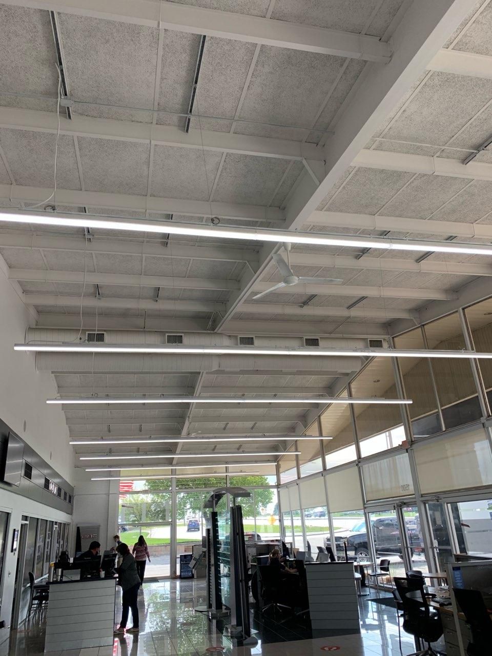 Interior of a salon with a high ceiling, bright linear lights, and several people visible.