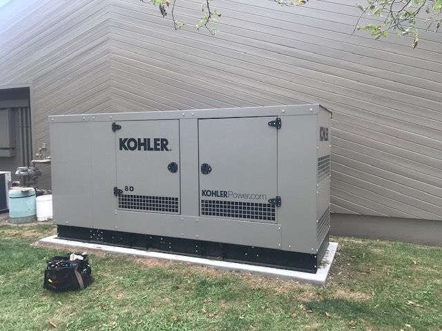 A large gray Kohler generator box is mounted on a concrete pad next to a house with brown siding.