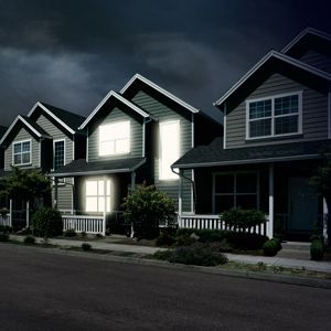 Row of houses at night, lit windows, street and dark cloudy sky.