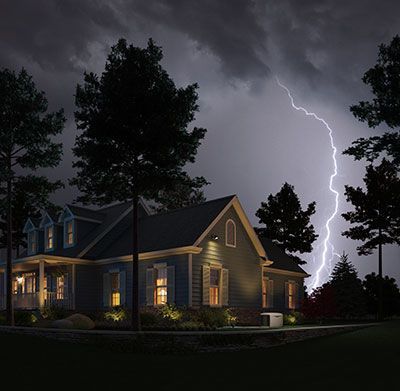 A house illuminated at night with lightning and dark trees in a storm.