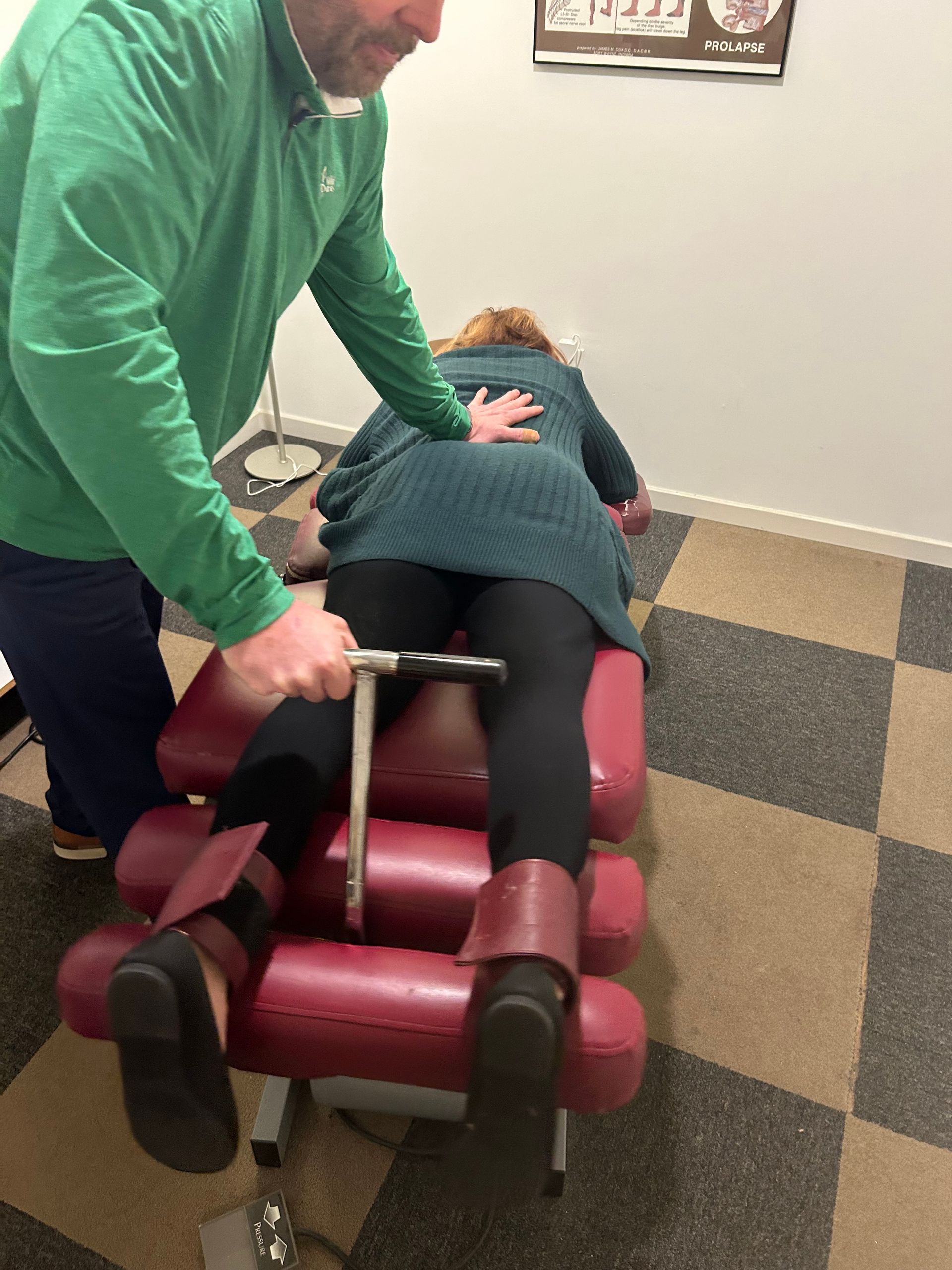 Chiropractor adjusting patient's back on a red adjusting table. Patient is lying prone.