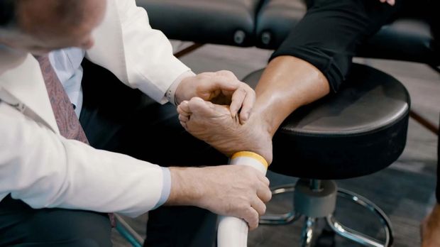 A doctor examines a patient's foot and ankle with a white support device.