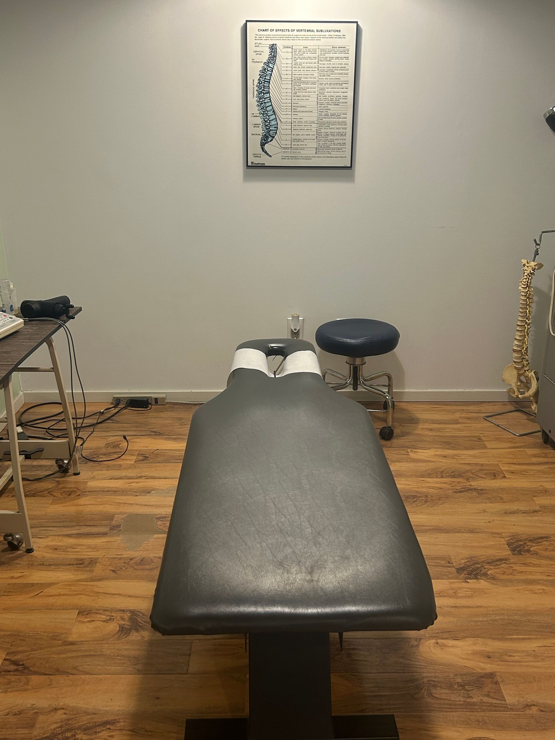 Chiropractor's office: table centered, anatomical chart on wall, stool, and medical equipment.