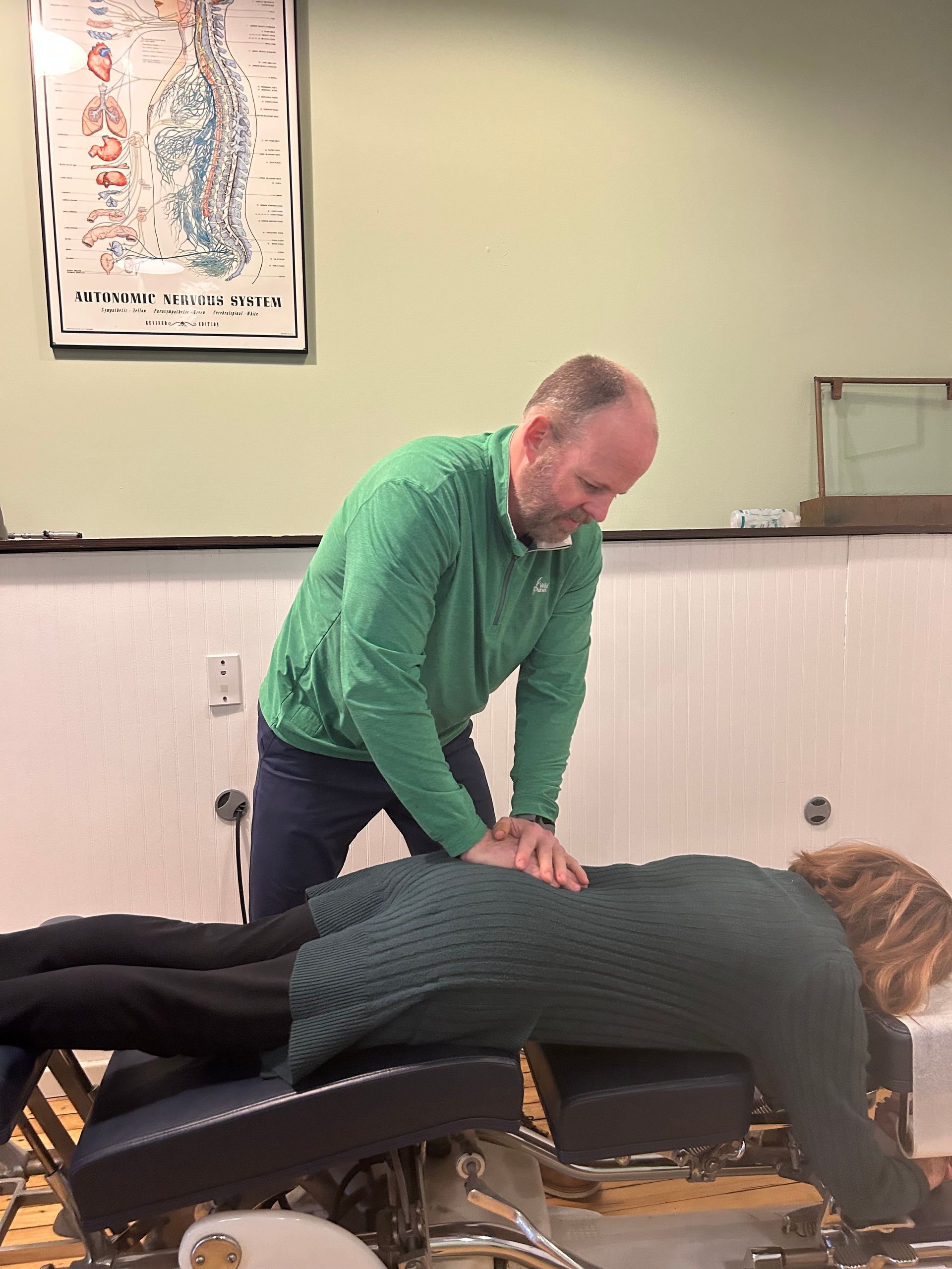 Man in green shirt adjusting a patient's back on an exam table.