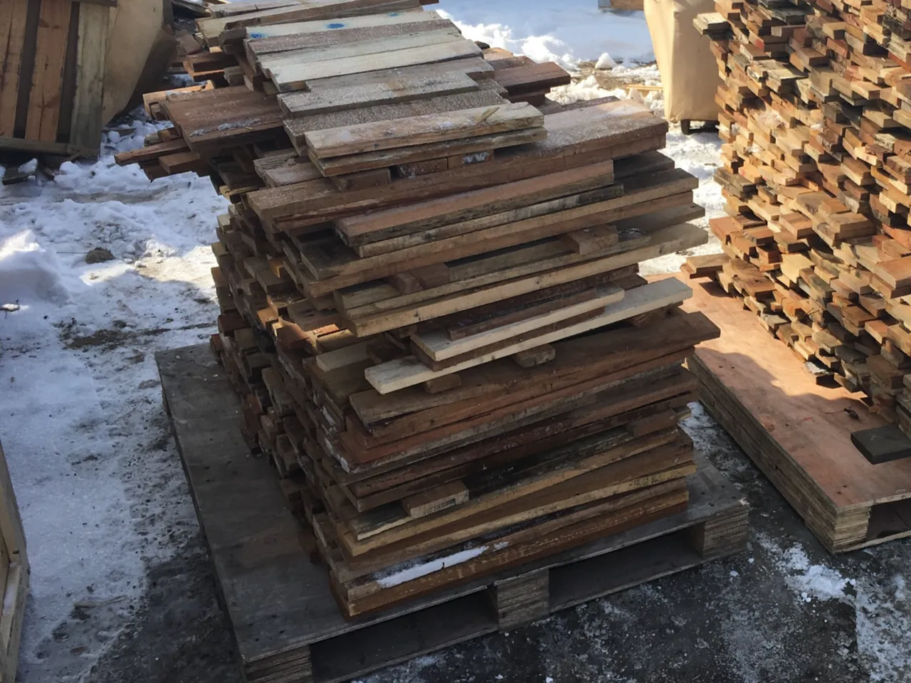 A stack of weathered wooden pallet boards resting on a pallet outdoors in the snow.