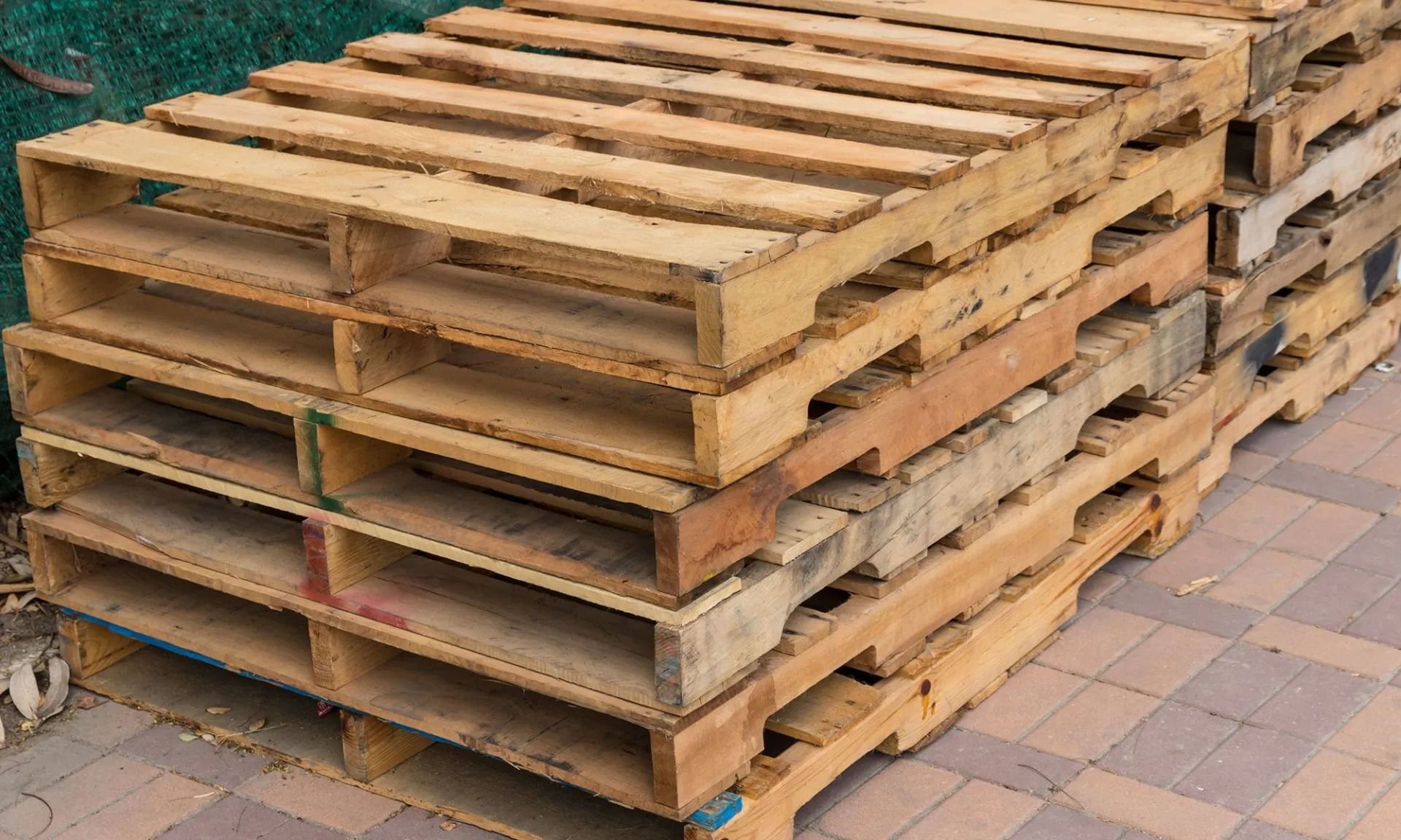 A stack of weathered, light brown wooden shipping pallets resting on a paved surface.