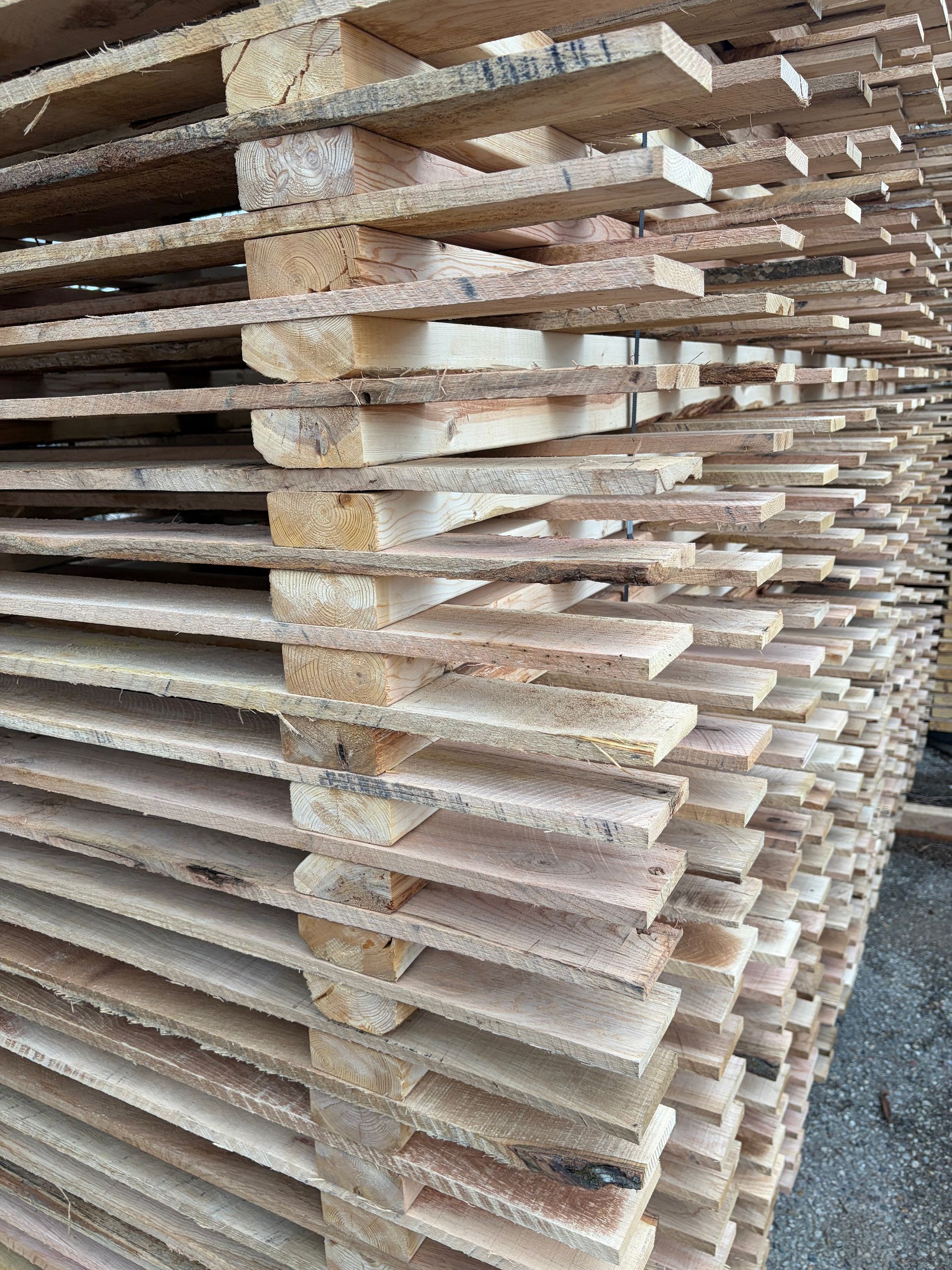 Stacked, rough-cut lumber planks layered with wooden spacers for drying in an outdoor setting.