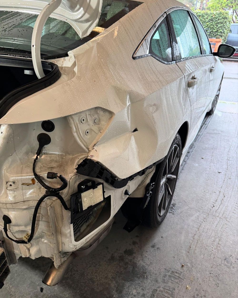 White car with significant rear damage, trunk open, outdoors.