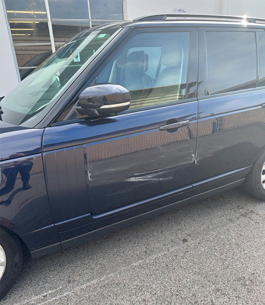 Blue Range Rover with a large dent in the side panel, parked outdoors.