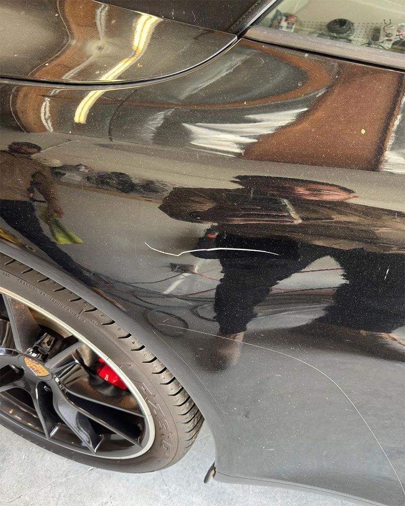 Black car with scratches on the side panel near the rear tire. Red brake caliper visible.