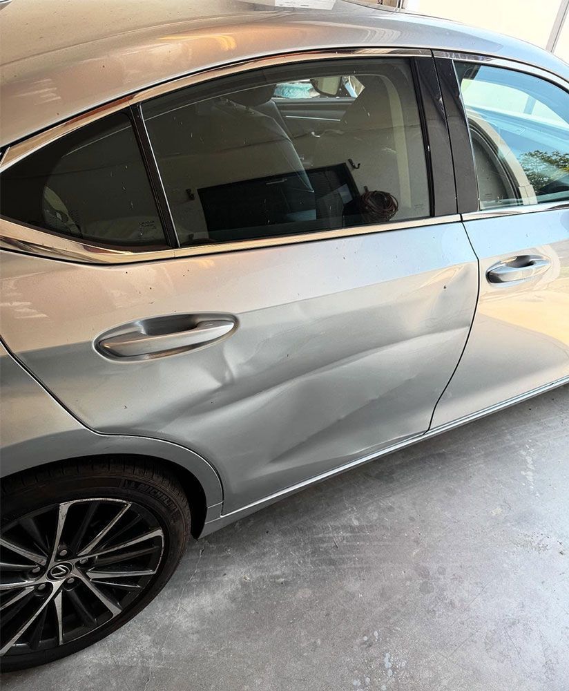 Silver car with dented rear passenger door.