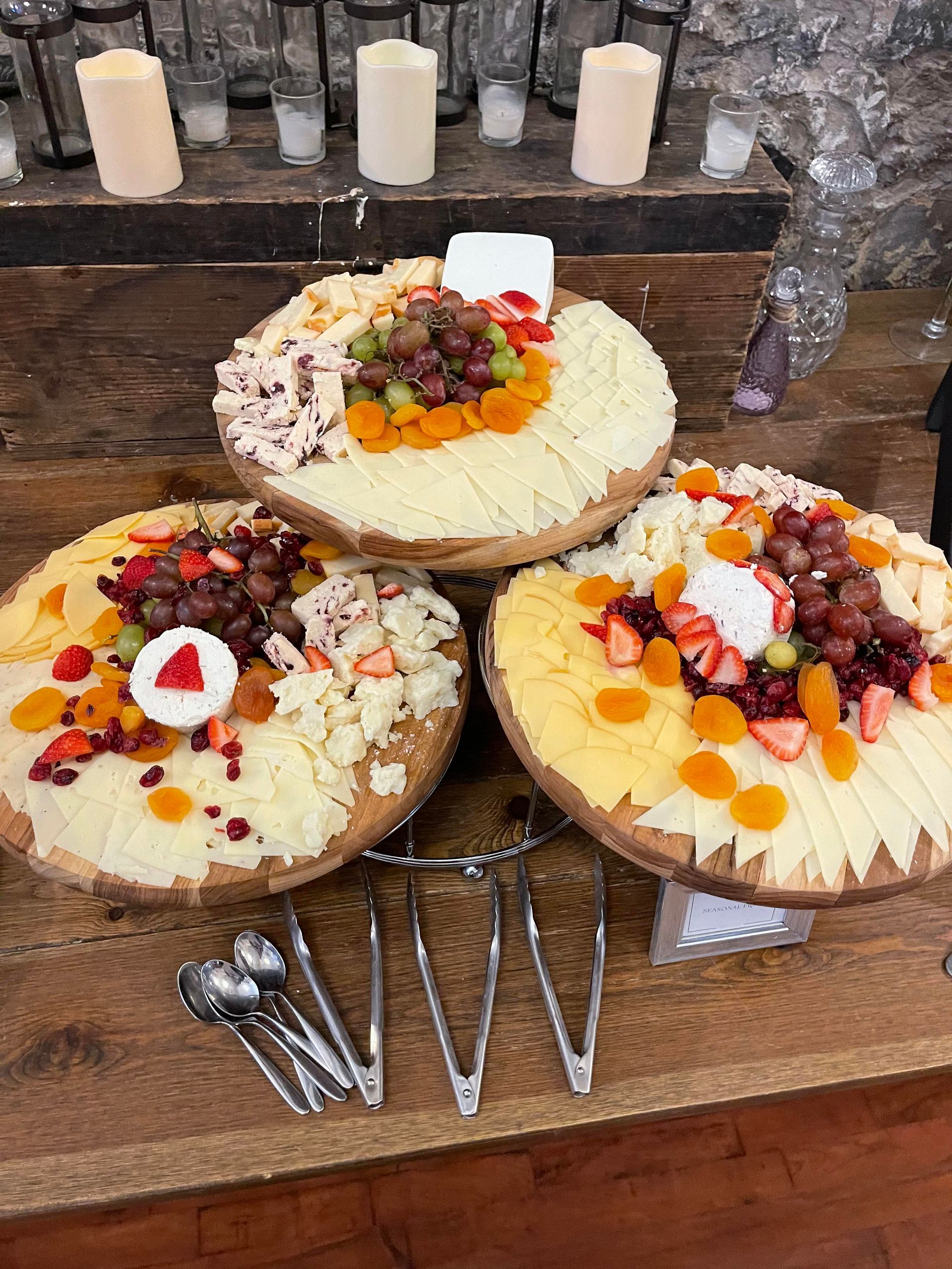 Three plates of cheese and fruit are sitting on a wooden table.