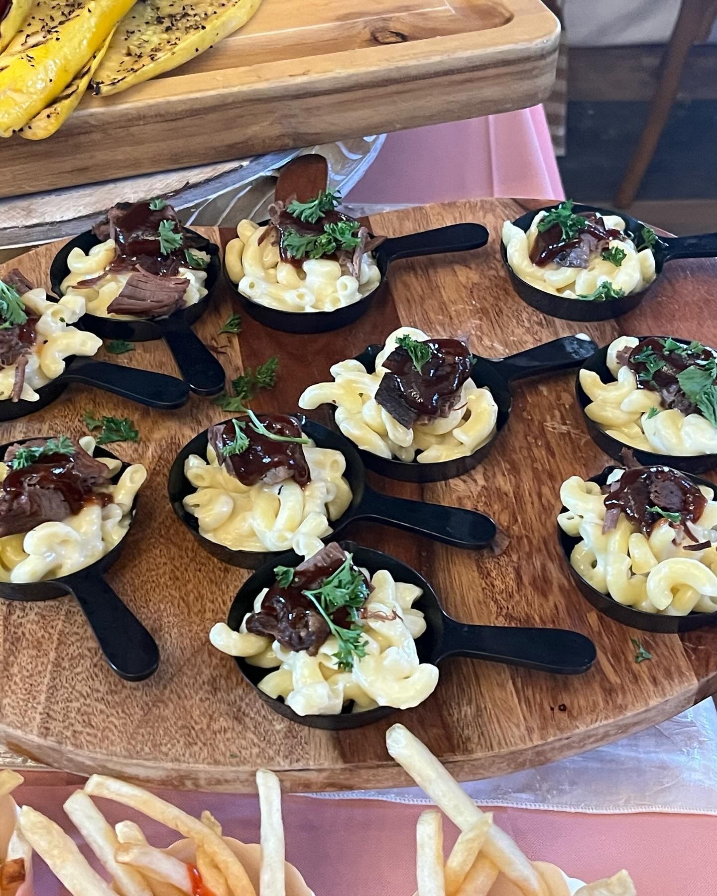 A wooden table topped with small pans of macaroni and cheese and french fries.