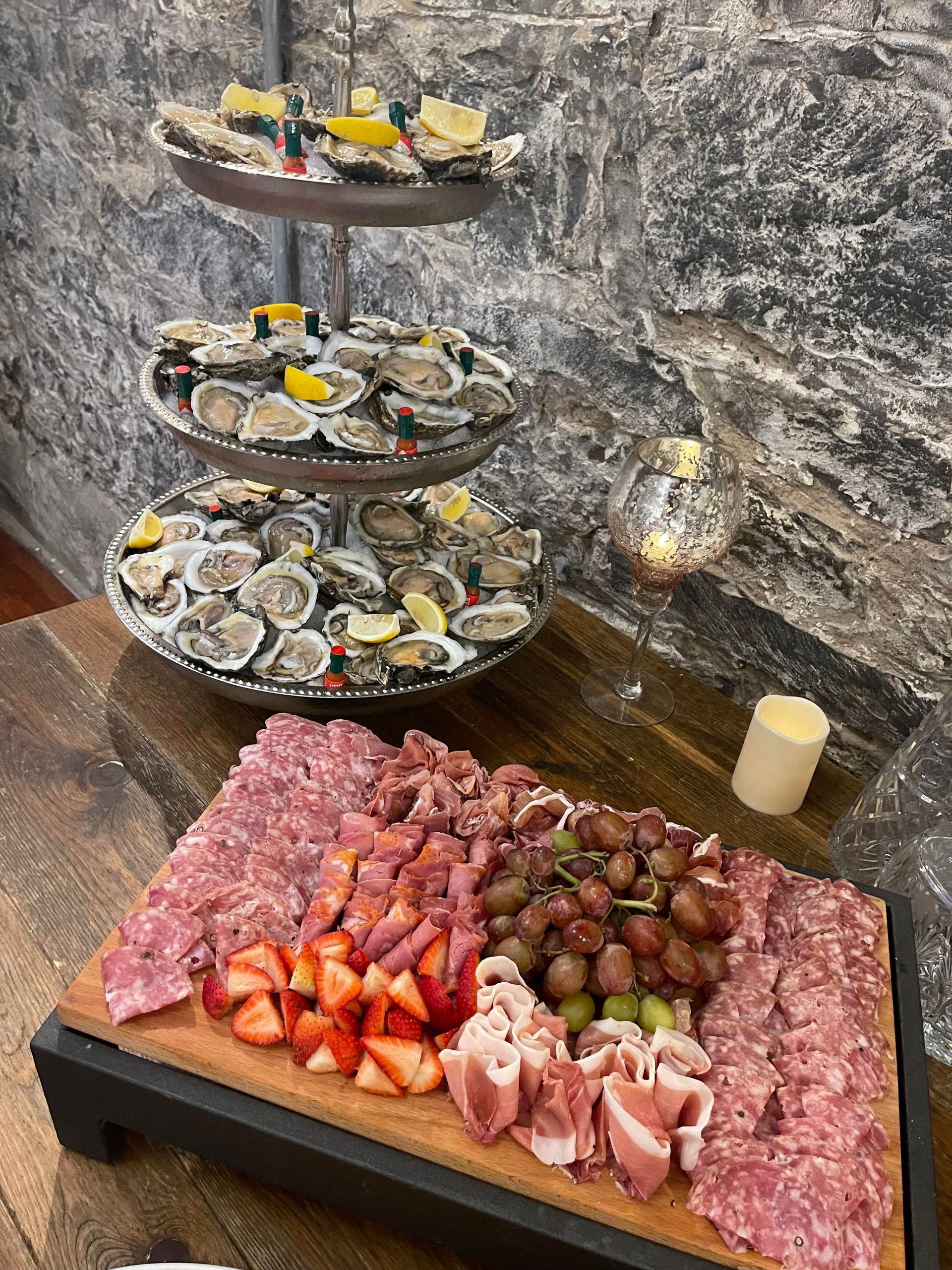 A wooden cutting board topped with meats and oysters on a table.