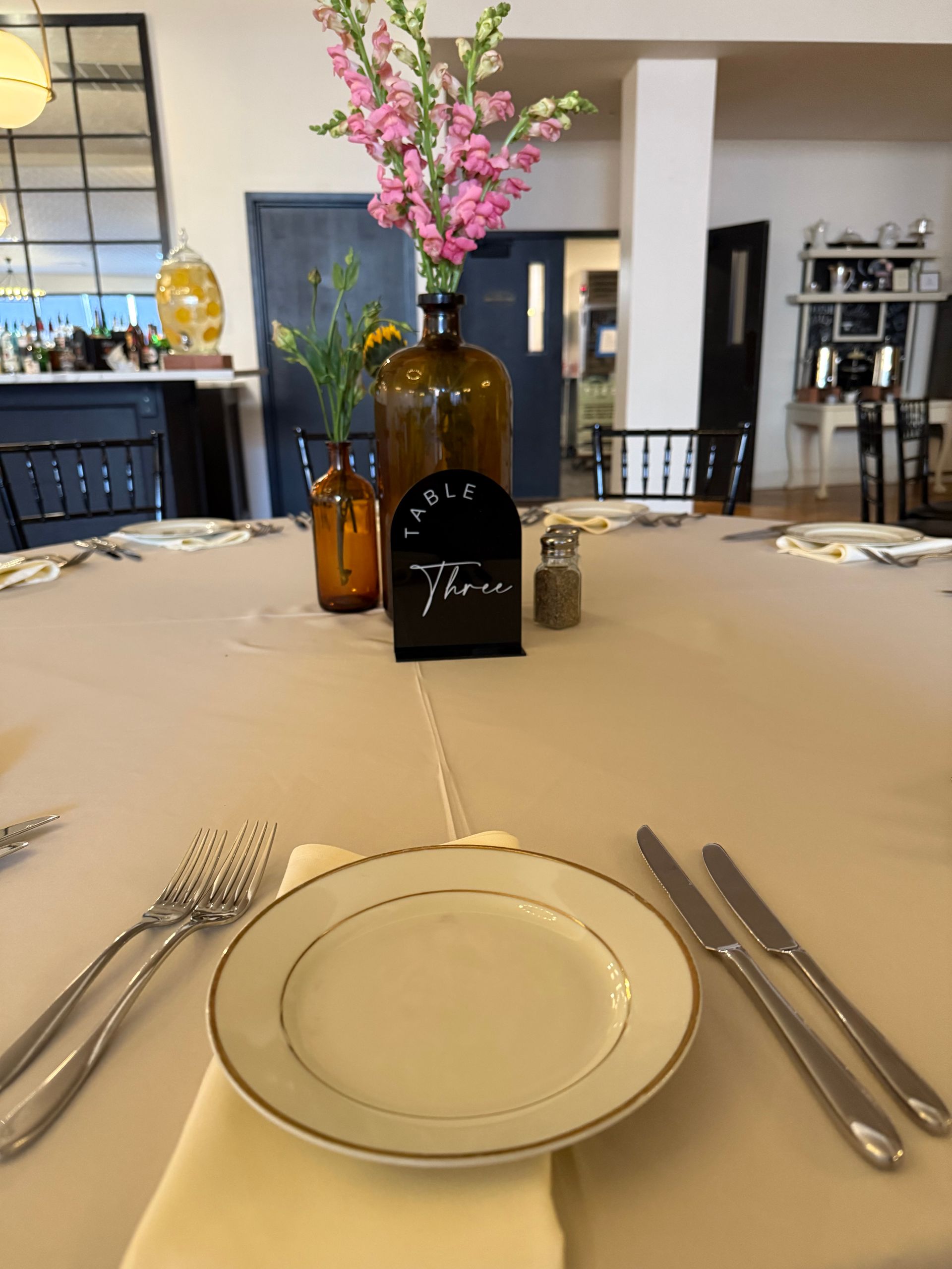 A table with a plate and silverware and a vase with pink flowers in it
