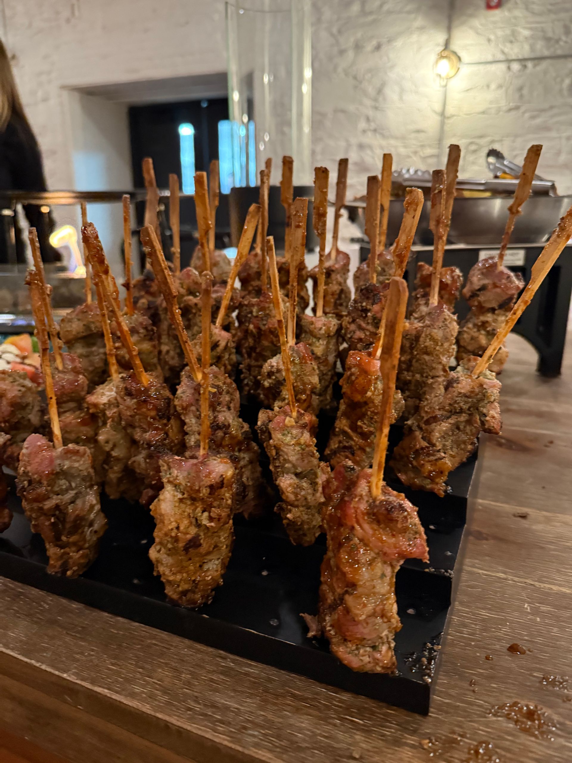 A bunch of meat on sticks on a tray on a table.