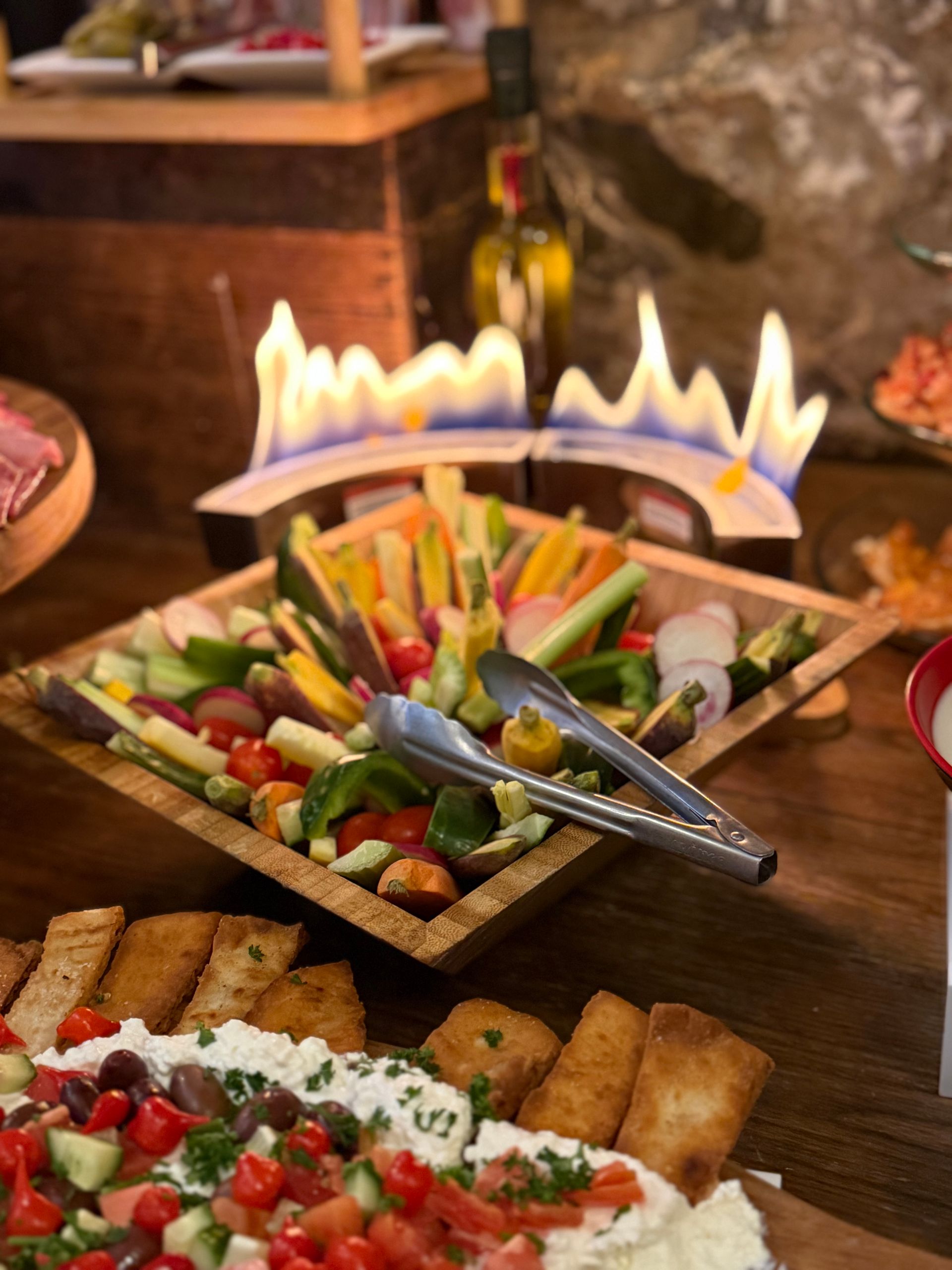 A buffet table with a bowl of vegetables and tongs on it