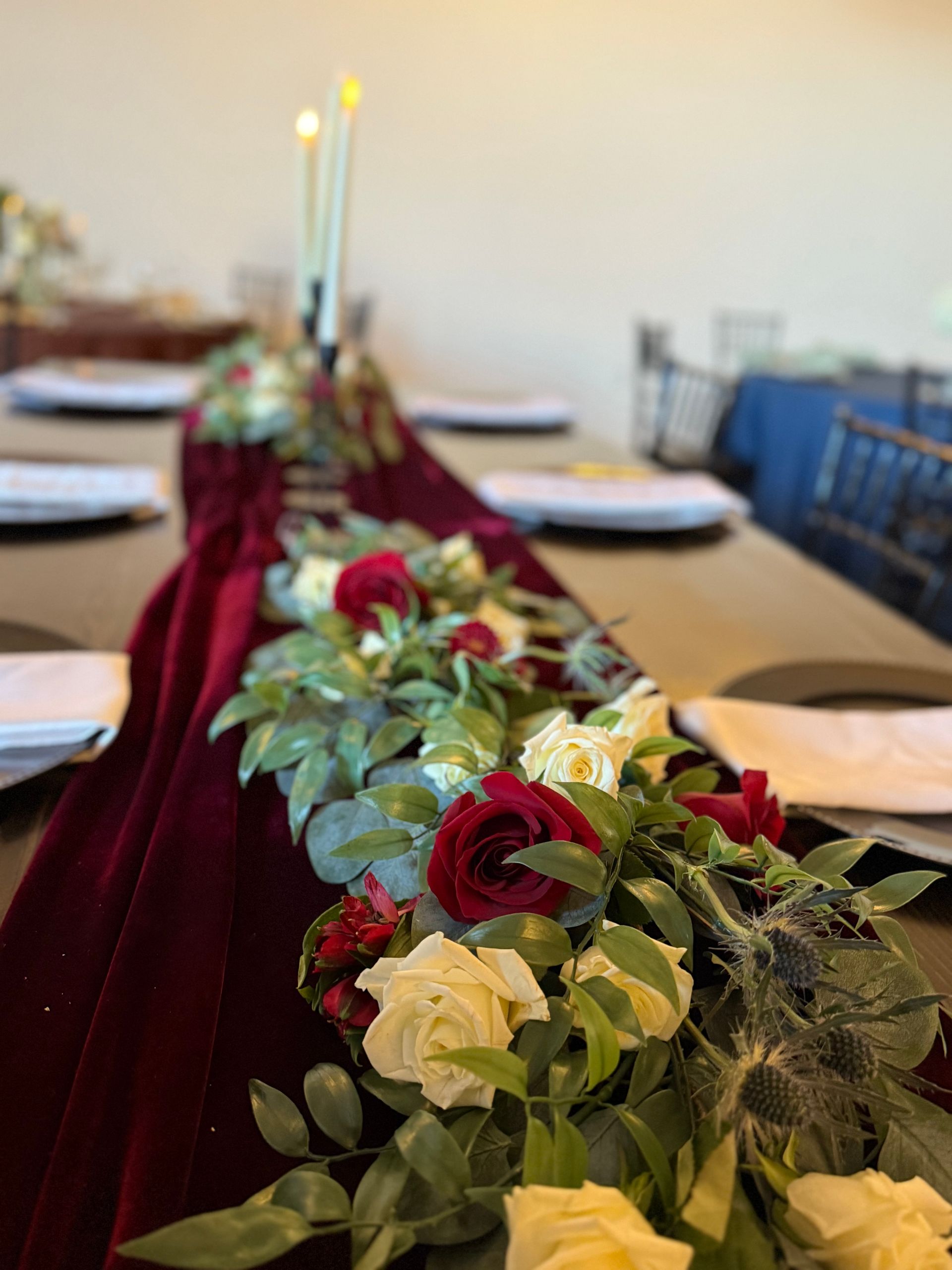 A long table with a red velvet table runner and flowers on it.