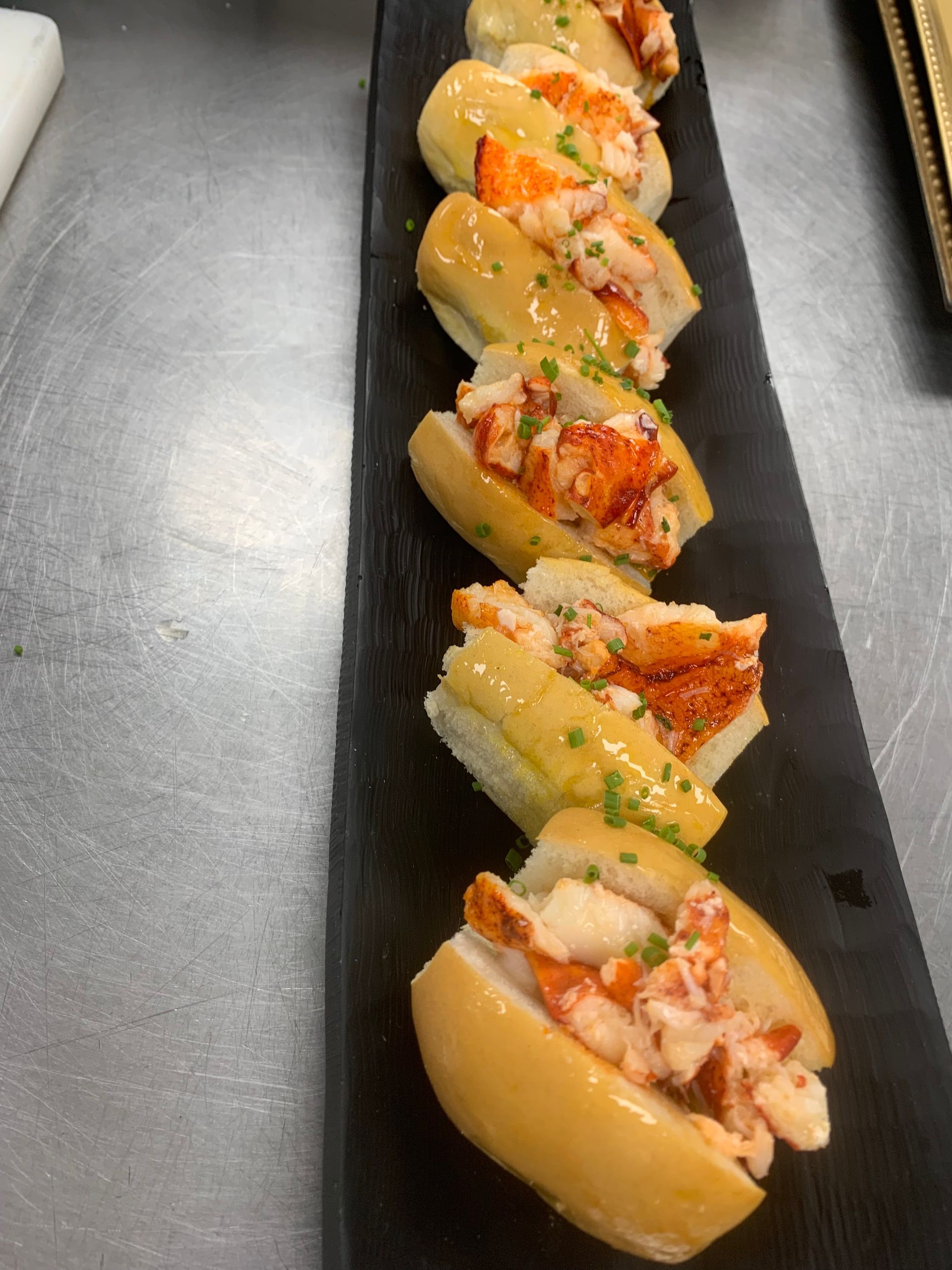 A row of lobster rolls on a black tray