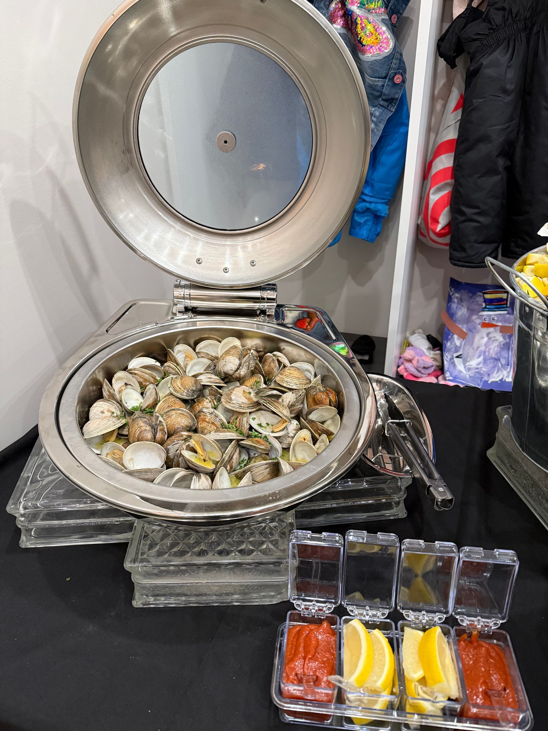 A buffet table with a bowl of clams and sauces on it.