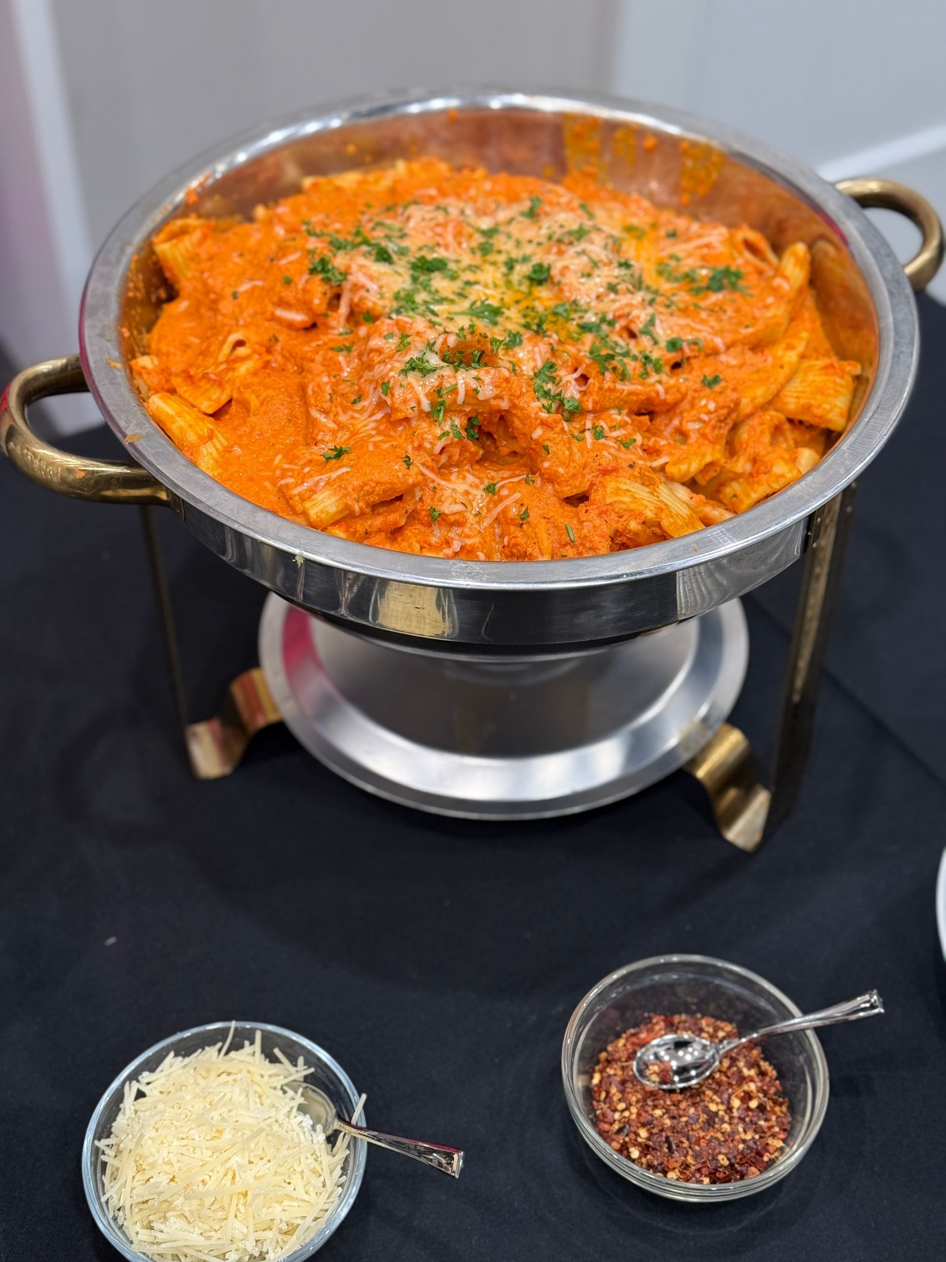 A pot of food is sitting on a table next to bowls of cheese and spices.