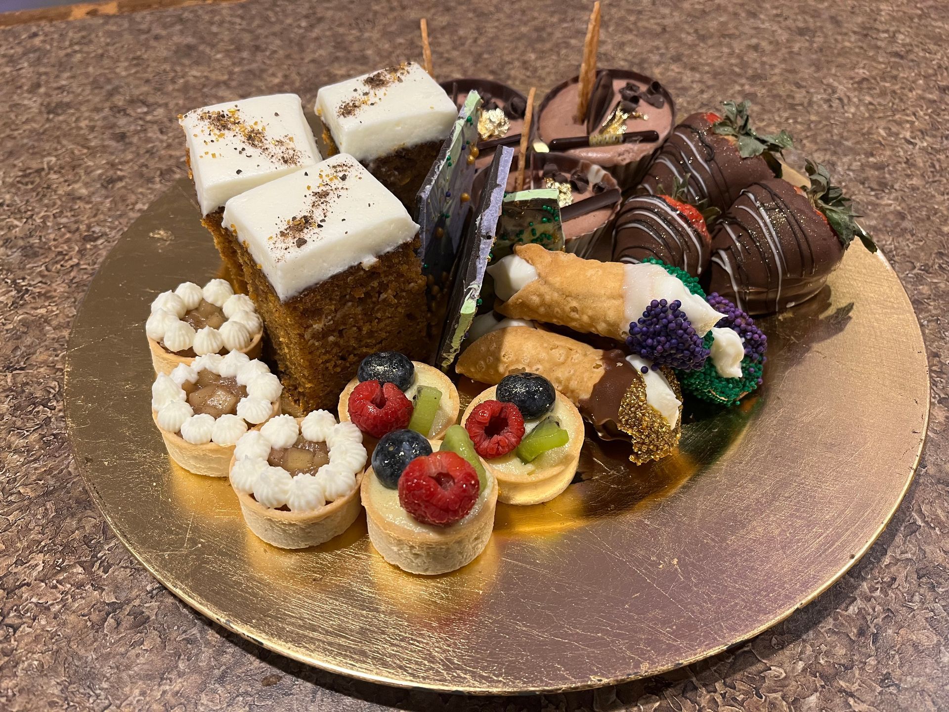 A gold plate topped with a variety of desserts on a table.