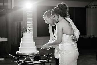 A bride and groom are cutting their wedding cake together in a black and white photo.