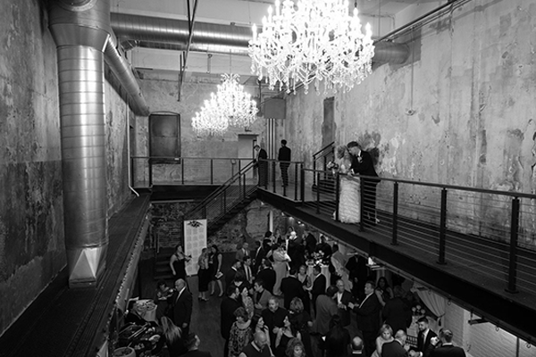 A black and white photo of a large room filled with people and chandeliers.