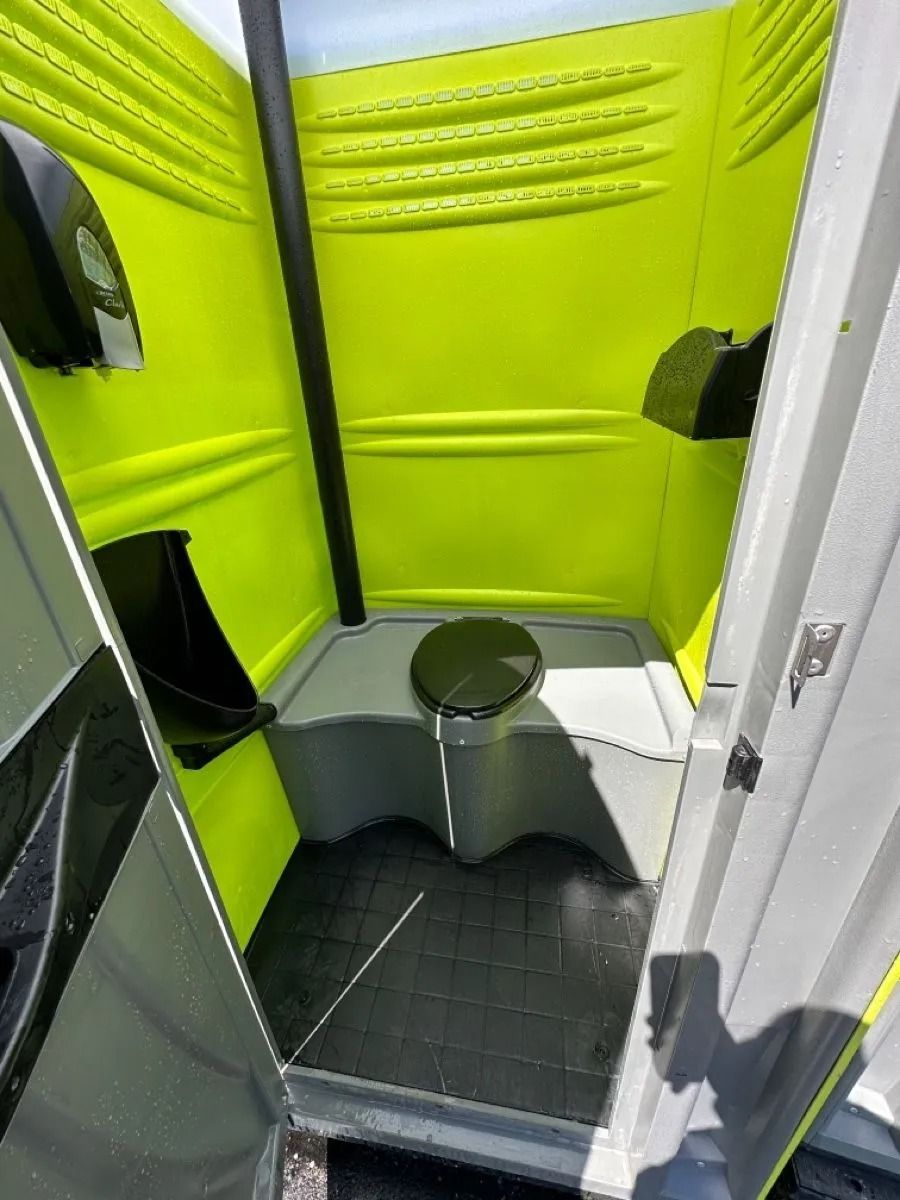 Interior of a portable toilet with bright lime-green walls, a black floor, and a central toilet seat with a black lid.