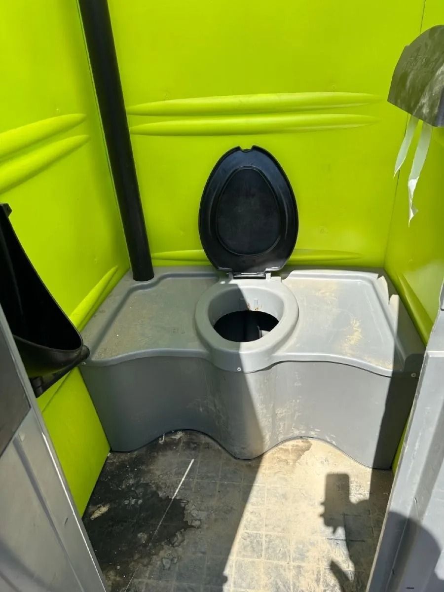 The interior of a bright lime green portable toilet with a grey plastic toilet seat and a small urinal on the left.