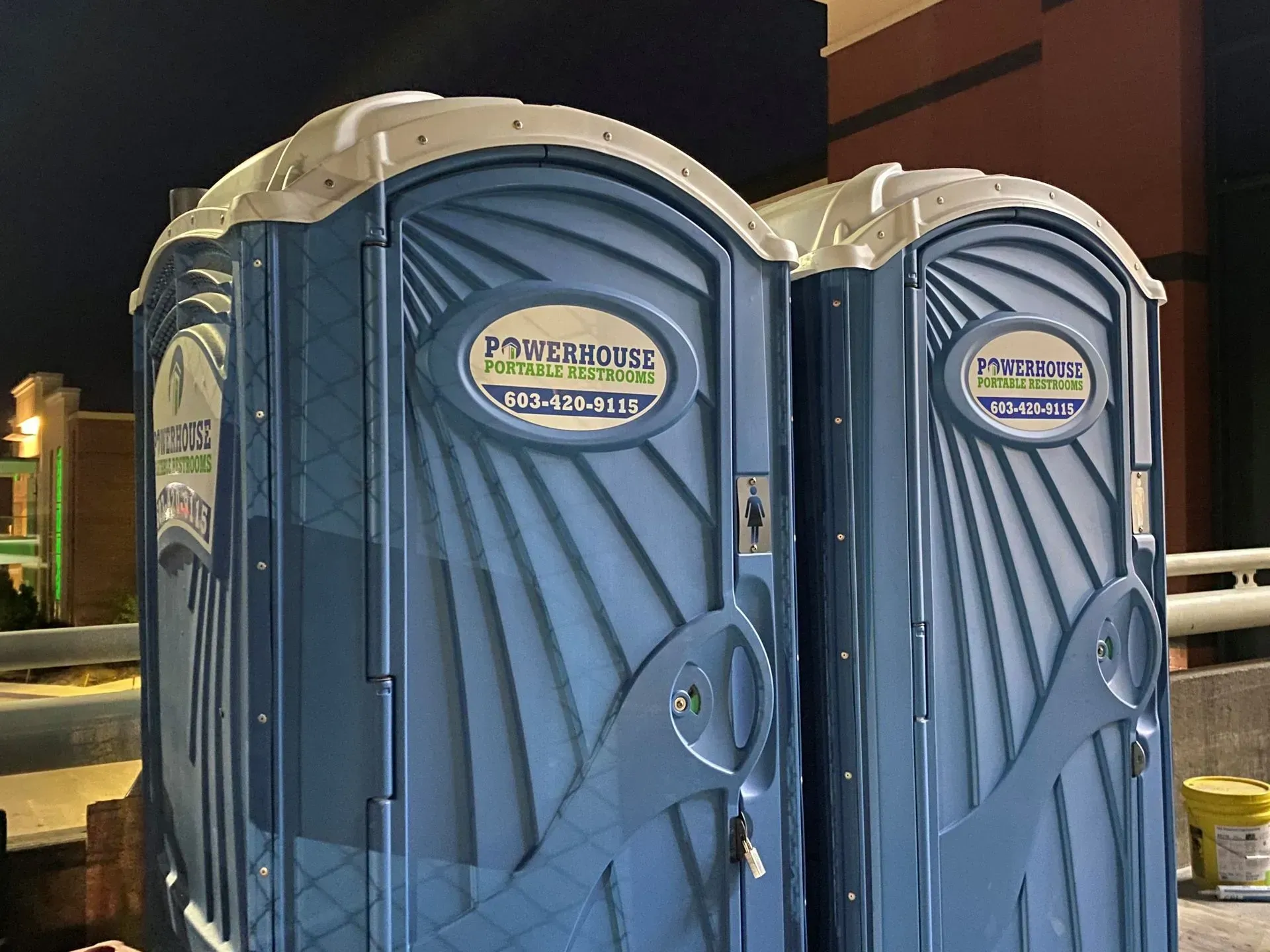 Two blue portable toilets standing side-by-side in an outdoor area at night.