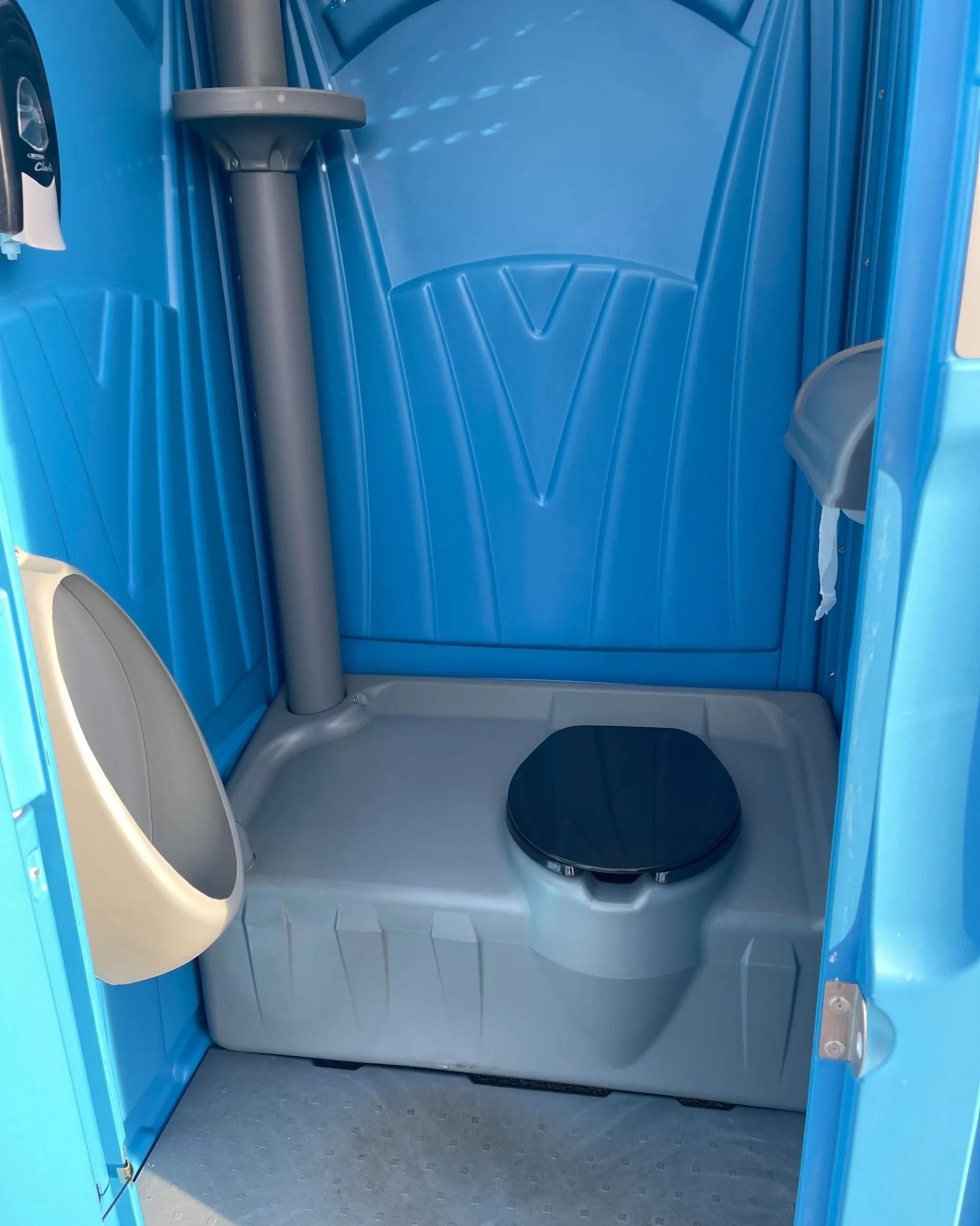 Interior of a bright blue portable toilet featuring a black seat, a grey base, and a wall-mounted urinal.
