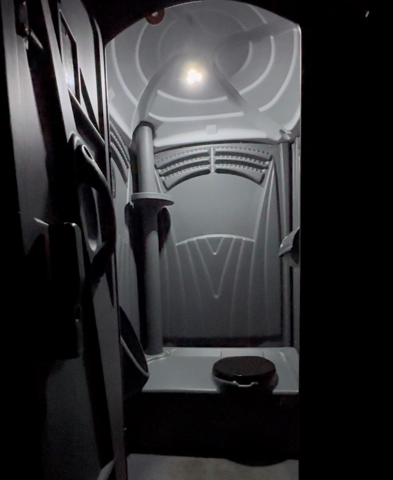 The interior of a dark, grey portable toilet with a toilet seat and a wall-mounted urinal.