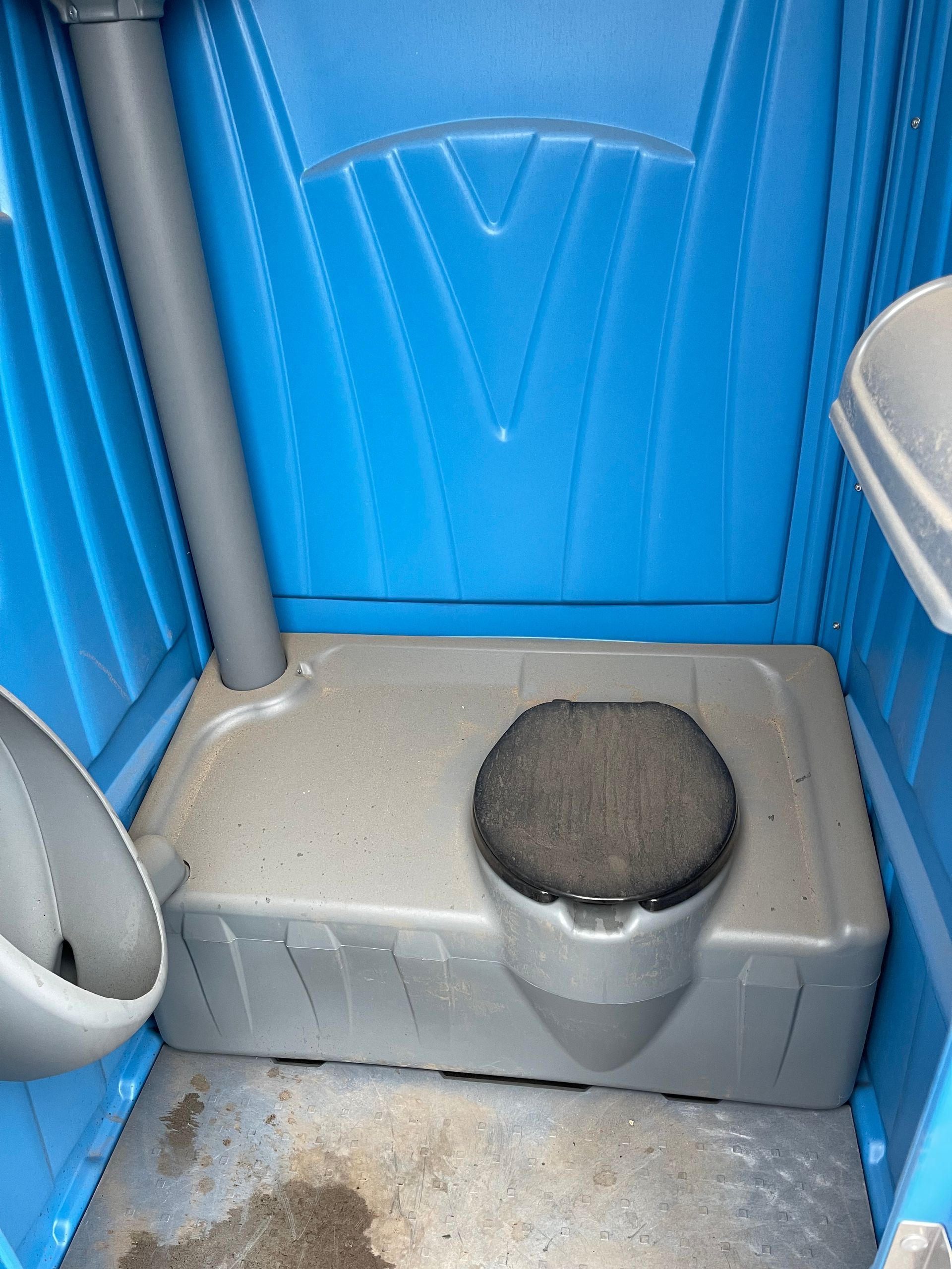 Portable toilet interior with blue walls, gray seat bench, and round black toilet opening on the floor