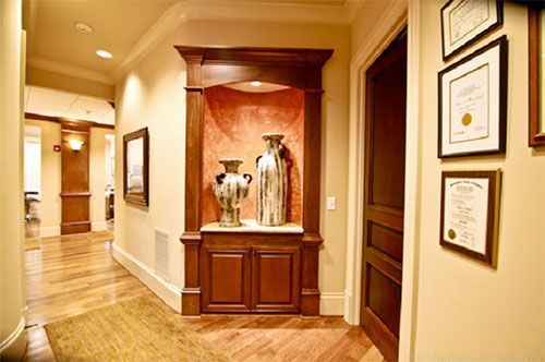 A hallway with a shelf with vases and certificates on the wall.