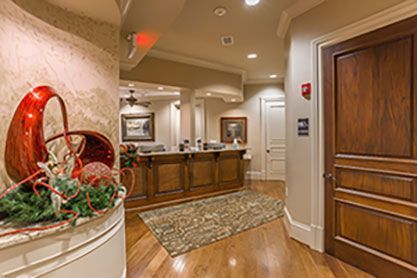 A hallway with a wooden floor and a wooden door leading to a reception desk.