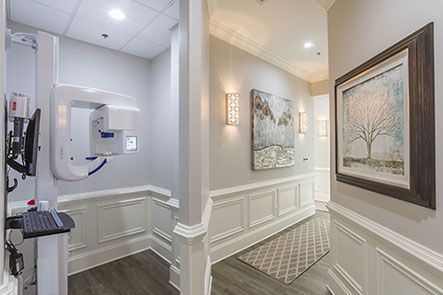 A hallway in a dental office with a x-ray machine and paintings on the wall.