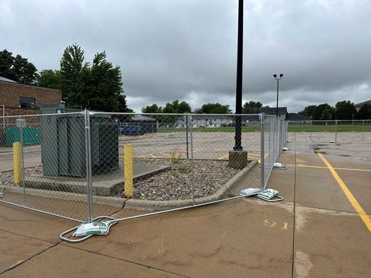 Chain link fence around a utility box in a parking lot. Gray, overcast sky.